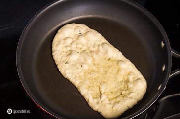 Frying the first side of the naan bread in a skillet. Recipe at Spoonabilities.com