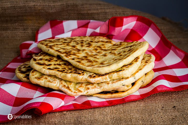 Six pieces of Homemade naan bread wrapped around a red checker napkin. Recipe at Spoonabilities.com