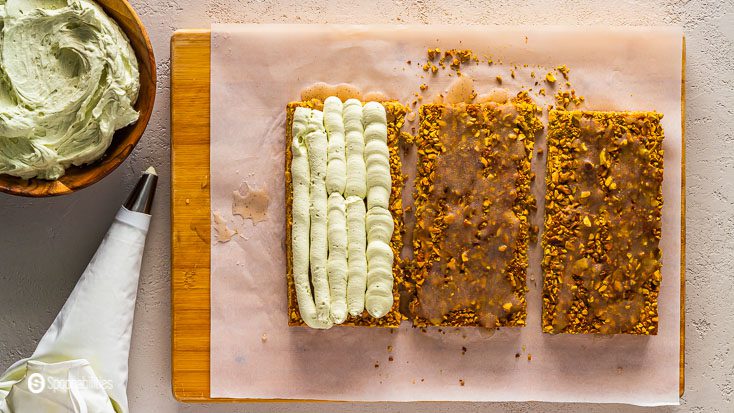 Wooden board and using a piping bag, top the first layer of pistachio tiramisu cake with the whipped mascarpone cream. Recipe at Spoonabilities.com