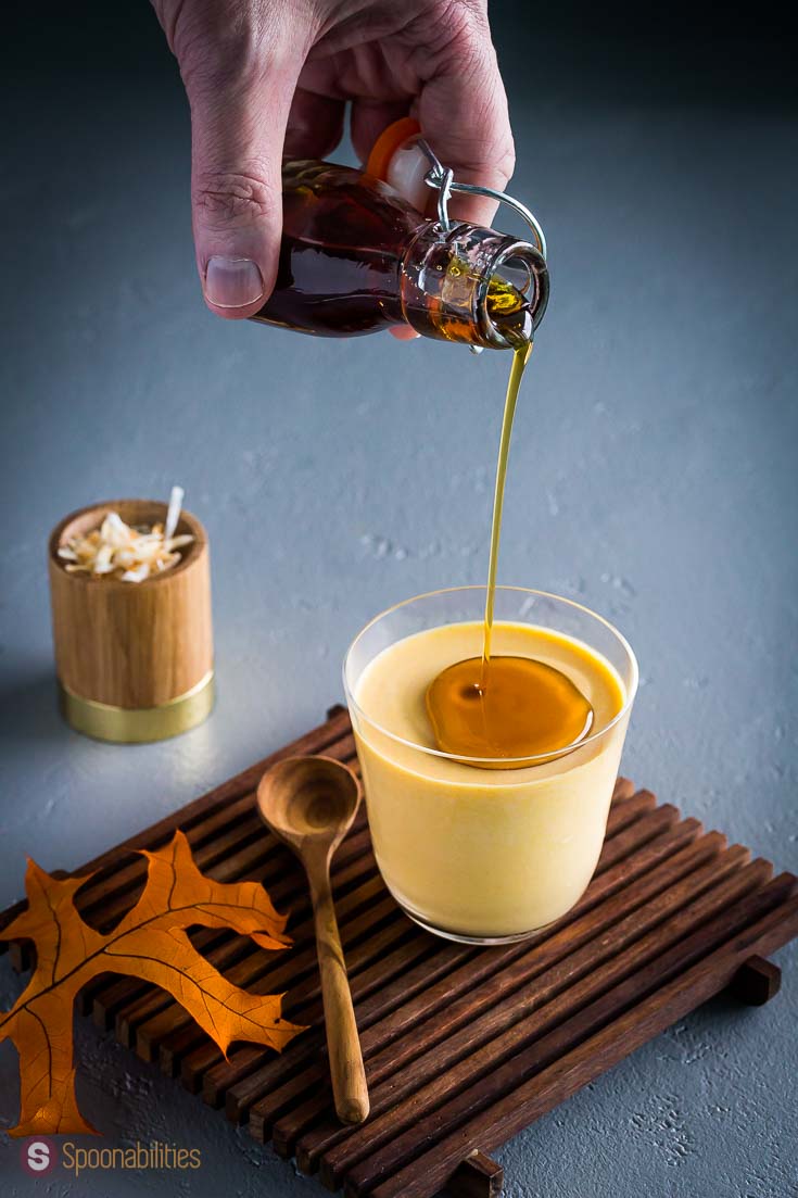 A hand pouring cinnamon-infused maple syrup on top of the pumpkin panna cotta. Recipe at Spoonabilities.com