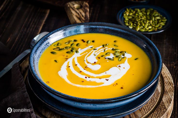 Close-up photo of a large blue bowl with the roasted butternut squash soup garnished with a drizzle of coconut cream, roasted pumpkin seeds, and smoked chili flakes. Recipe at Spoonabilities.com