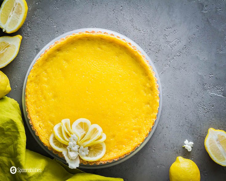 Citrus tart garnished with lemon slices. The photo is style with whole lemons and lemon halves. More about this tart recipe at Spoonabilities.com