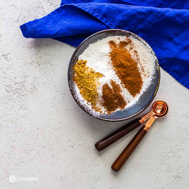 Dry ingredients in a small blue bowl for for the pistachio tiramisu: all-purpose flour, cinnamon, baking powder, ginger, nutmeg, and sea salt. Recipe at Spoonabilities