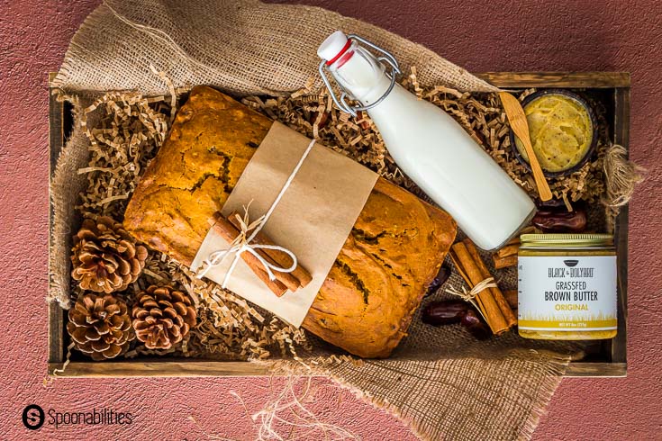 Wooden crate prepare for a gift with a loaf of date pumpkin bread with hazelnut. The bread is wrapped with a brown paper and in the crate you will find a bottle of milk, a jar of brown butter, and fall décor. Recipe at Spoonabilities.com