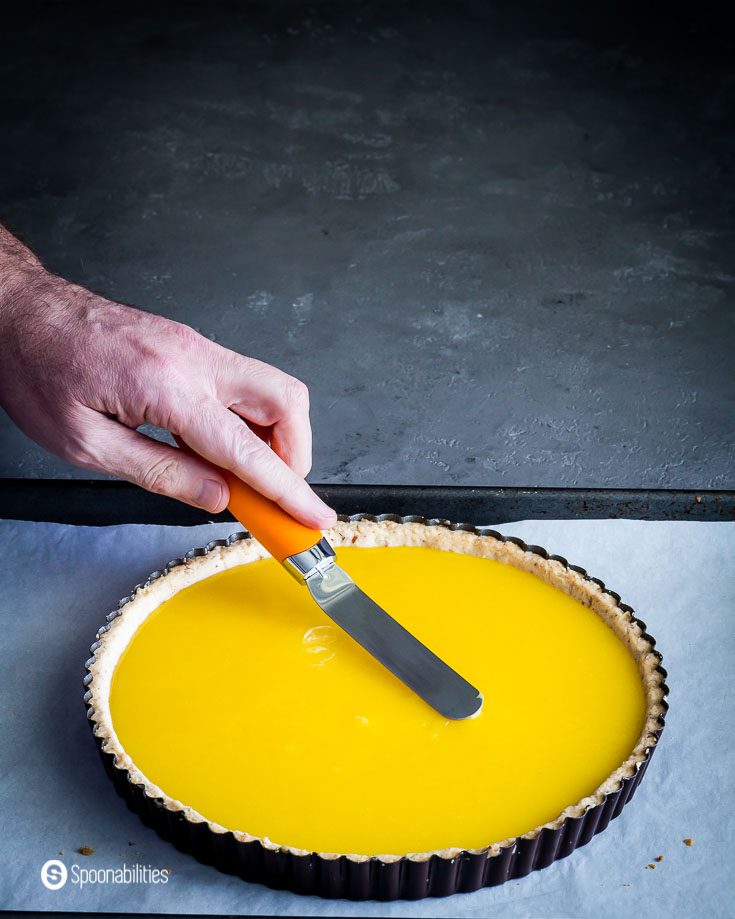Prebake Lemon tart with a hand, smoothing out the top after pouring the lemon curd to the par-baked crust. Recipe at Spoonabilities.com