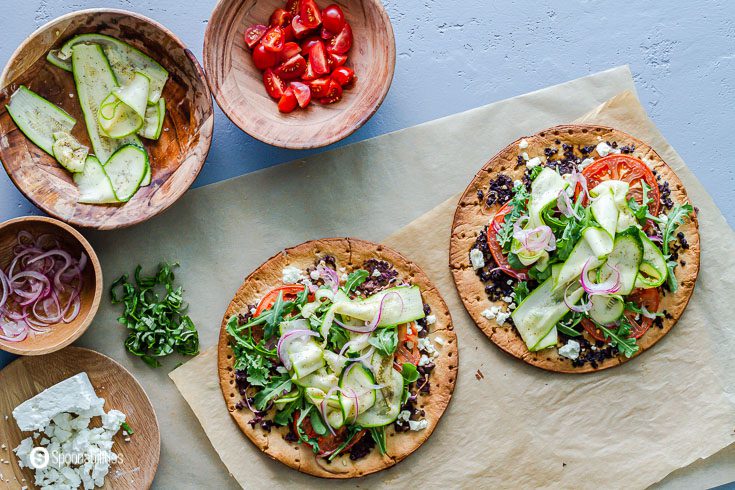 Two cauliflower pizza crust with olive bruschetta, feta cheese, tomatoes, arugula, red onions, and basil. More about this recipe at Spoonabilities.com