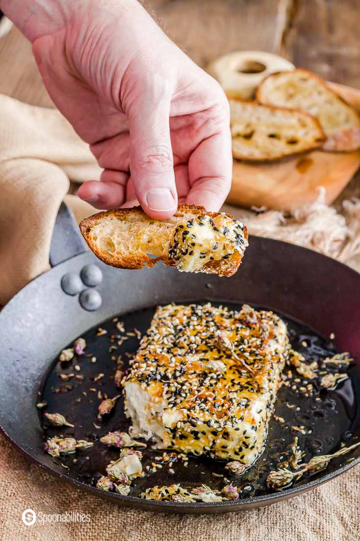 A hand with a piece of bread scooping out some of the sesame crusted fried feta cheese. Recipe at Spoonabilities.com