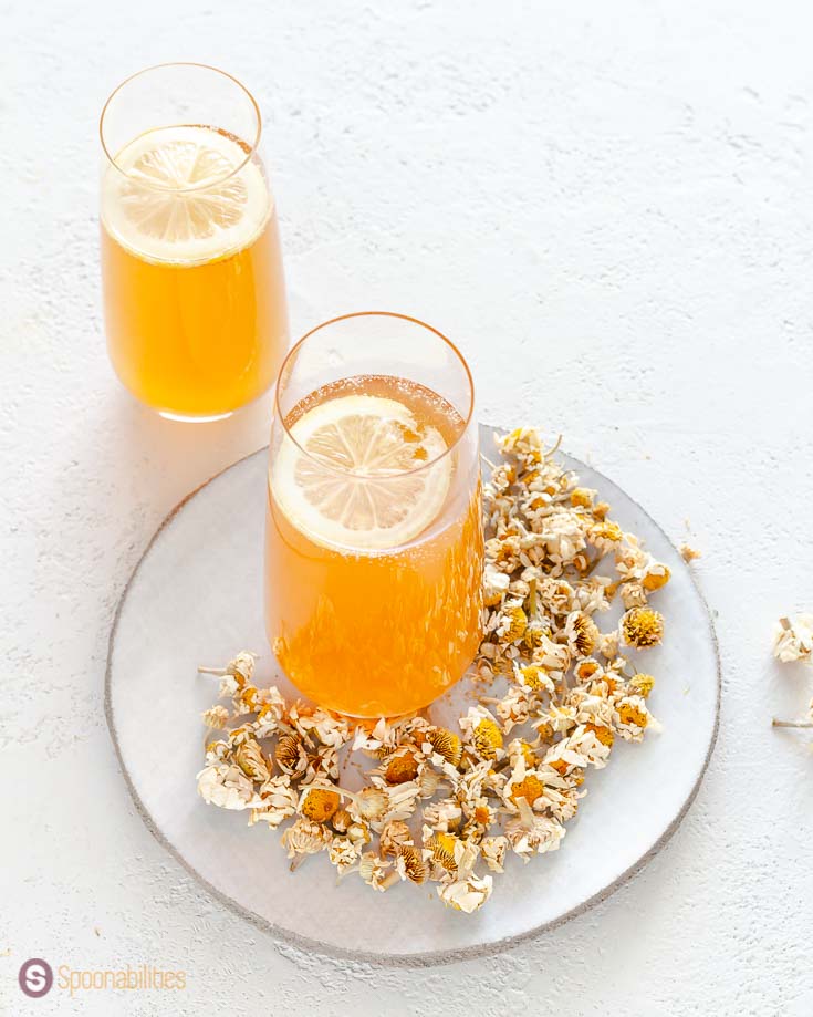 A close-up photo showing some of the inside of the glass with the vodka punch. The glass is on top of a round white plate with chamomile flowers. Recipe at Spoonabilities.com