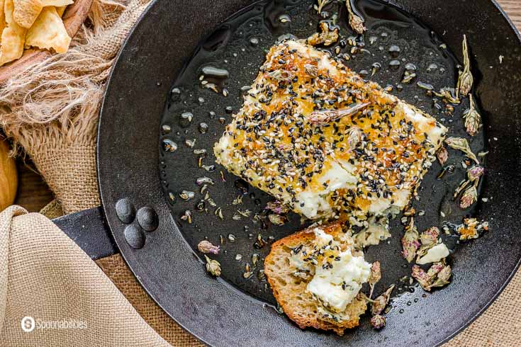 Close up of the sesame crusted feta cheese with a toasted bread and a piece of the cheese on top. Recipe at Spoonabilities.com