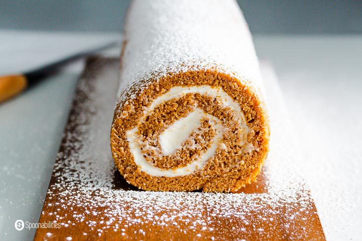 A close-up photo with the beautiful end of the roll cake on a wooden board showing the cake's inside filled with sweet cream cheese filling. Recipe at Spoonabilities.com