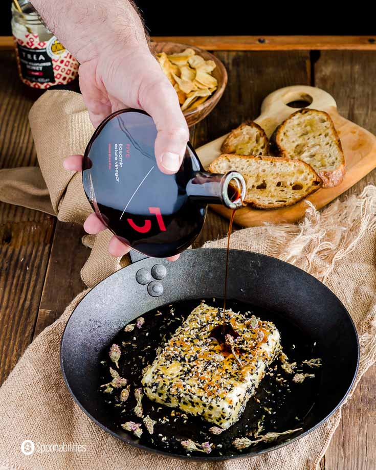 A hand pouring Five balsamic vinegar on top of the crusted pan fried feta cheese. Recipe at Spoonabilities.com