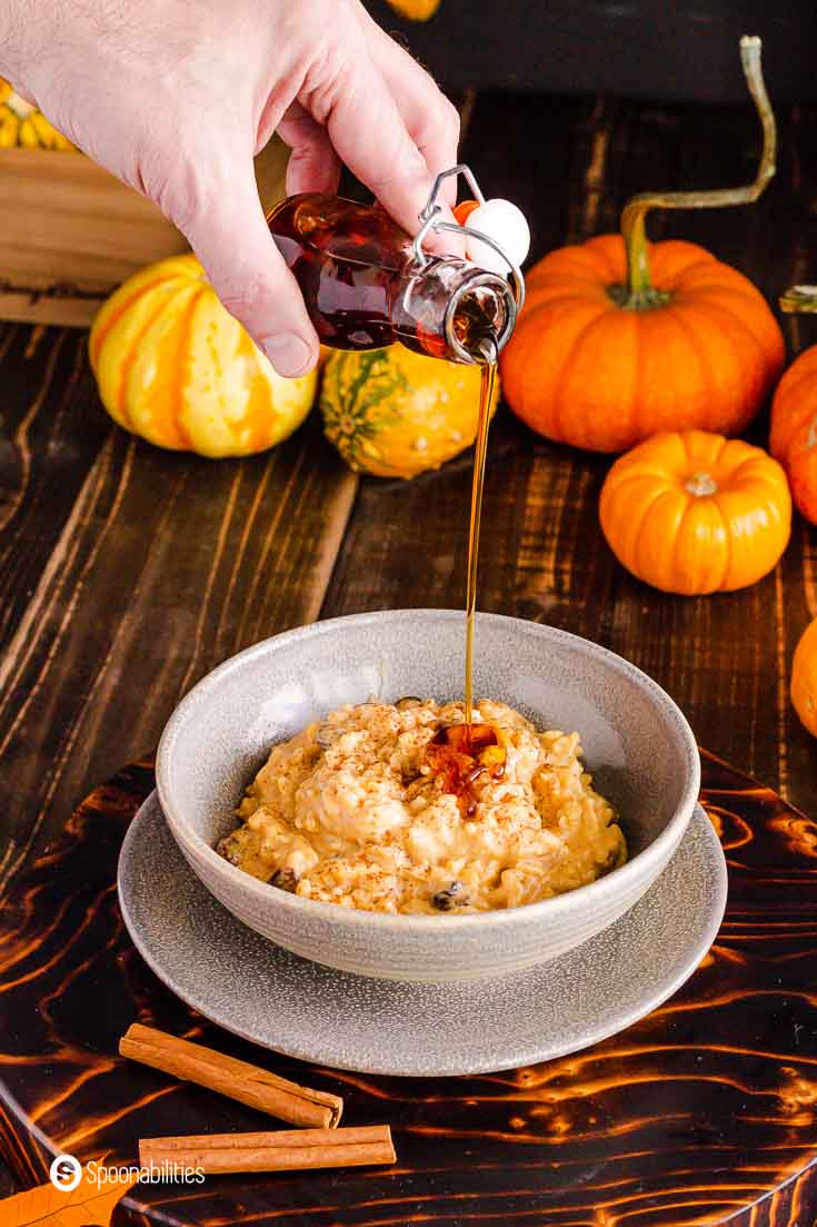 A hand pouring Vermont maple syrup on top of a bowl with coconut pumpkin rice pudding. More details at Spoonabilities.com