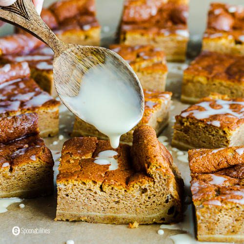 A few pieces of pumpkin magic cake with a wooden spoon drizzling Vermont Maple Syrup Glaze. Recipe at Spoonabilities.com