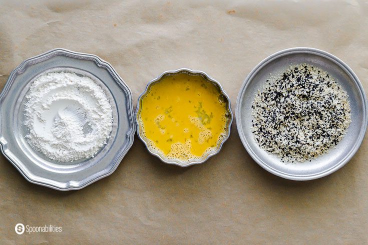 Three bowls : one with flour, the second with a beaten egg, and the last one with a mix of panko bread, white and black sesame seeds. Recipe at Spoonabilities.com