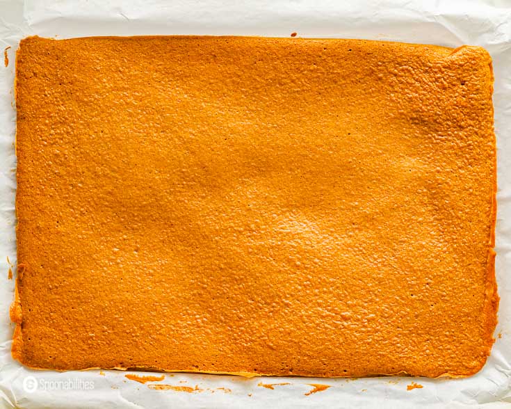 Pumpkin cake getting cool off on a parchment paper before it's been roll-up. Recipe at Spoonabilities.com