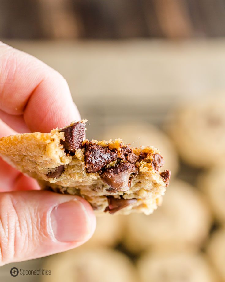 A hand holding a half of a chocolate chip cookie showing the soft chocolate chips inside the cookie. Recipe at Spoonabilities.com