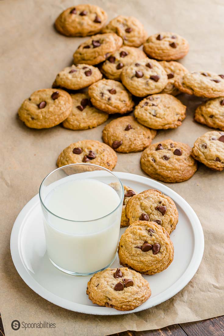 White plate with a glass of milk on top and four Nestle tollhouse cookies next to the glass. The plate is on top of a brown parchment paper. Recipe at Spoonabilities.com
