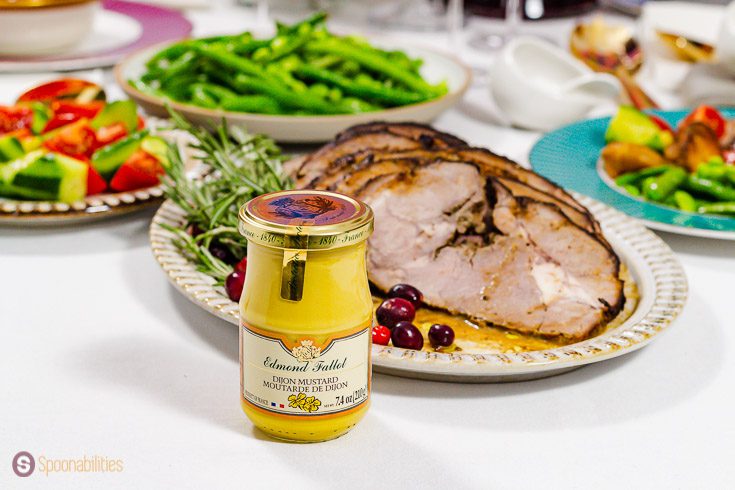 A jar of Edmond Fallot traditional Dijon Mustard in front of a oval plate with roasted lamb. Recipe at Spoonabilities.com