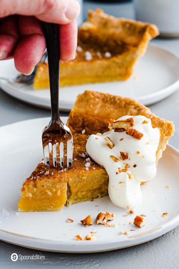 Close up photo of the salted maple pie with whipped cream and flaky sea salt. A fork getting a piece of the pie. Recipe at Spoonabilities.com