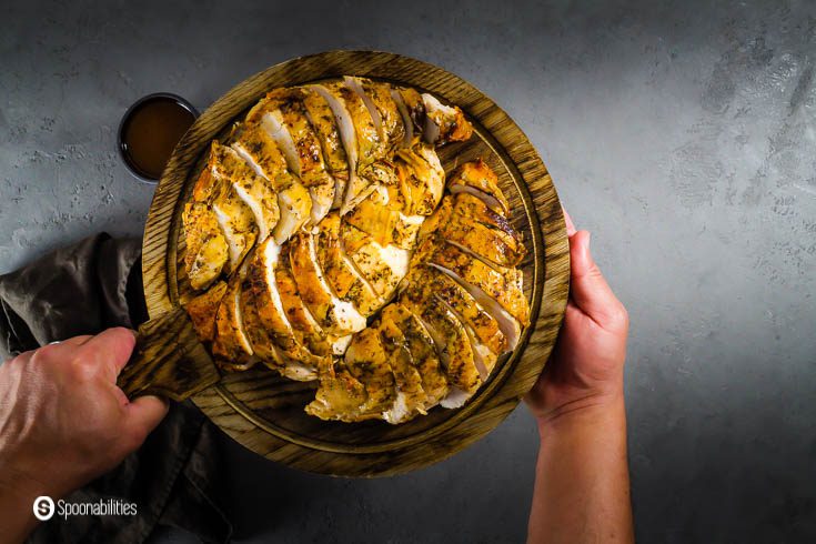 Two hands holding a wooden serving board with the sliced turkey breast seasoned with red chili brown butter and herbs. Recipe at Spoonabilities.com