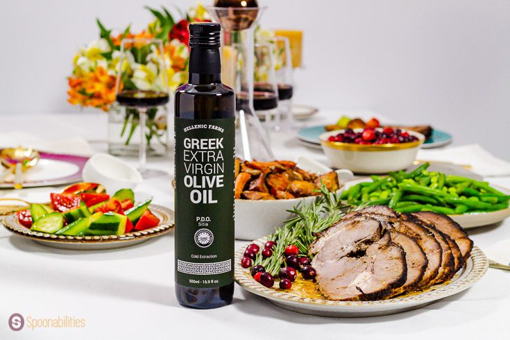 A bottle of Hellenic Farms Extra Virgin Olive oil. The bottle is in front of a plate with roasted leg of lamb garnished with fresh rosemary and fresh cranberries. Recipe at Spoonabilities.com