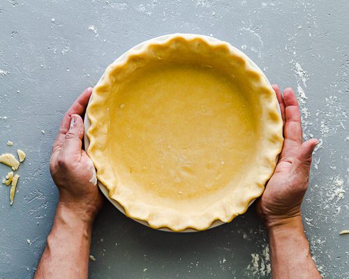 Two hands are holding the pie dish with the crust shaped. Ready to go into the refrigerator for 30 minutes. Spoonabilities.com