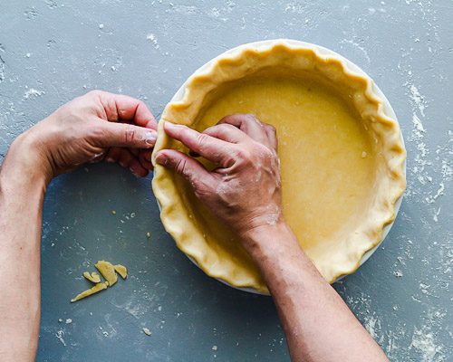 This photo has the pie dough crust in the pie dish and two hands making the pretty edges using the three fingers to shape the dough crust. Recipe at Spoonabilities.com