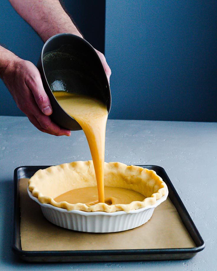 Two hands holding a flexible bowl and pouring the pie filling into the all butter pie crust. Recipe at Spoonabilities.com
