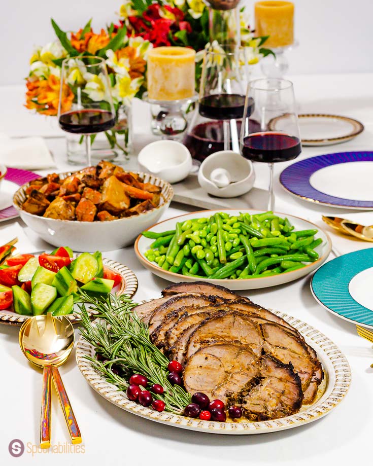 Table setting for a holiday dinner with an oval plate in the center with slices of leg of lamb roasted with Dijon mustard, lavender honey, olive oil, fresh herbs, and garlic. Recipe at spoonabilities.com