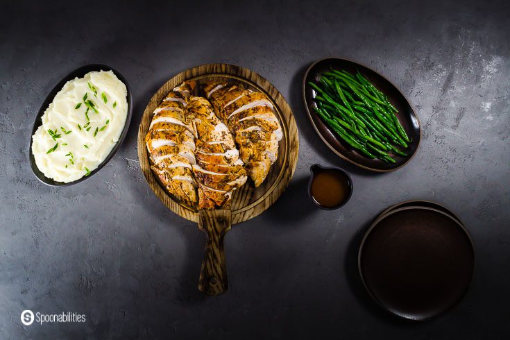 Overhead photo with three serving dishes. In the center in a wooden board the roasted turkey breast sliced, on the right side steam green beans, and on the left side mashed potatoes. Recipe at spoonabilities.com