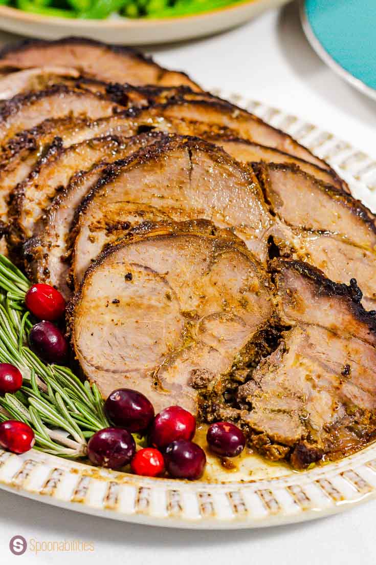 Close up of the sliced roasted leg of lamb on a oval plate. Garnished with fresh rosemary and cranberries. Recipe at Spoonabilities.com