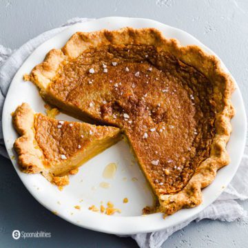 White round pie dish with a salted maple pie with flaky sea salt on top. One piece cut out and another piece missing from the dish. Recipe at Spoonabilities.com