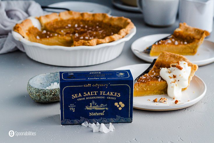 A blue box presentation of the Flaky Sea Salt from Missolonghi-Greece. In the background a pie dish and two small plates with a slice of maple pie. Recipe at Spoonabilities.com