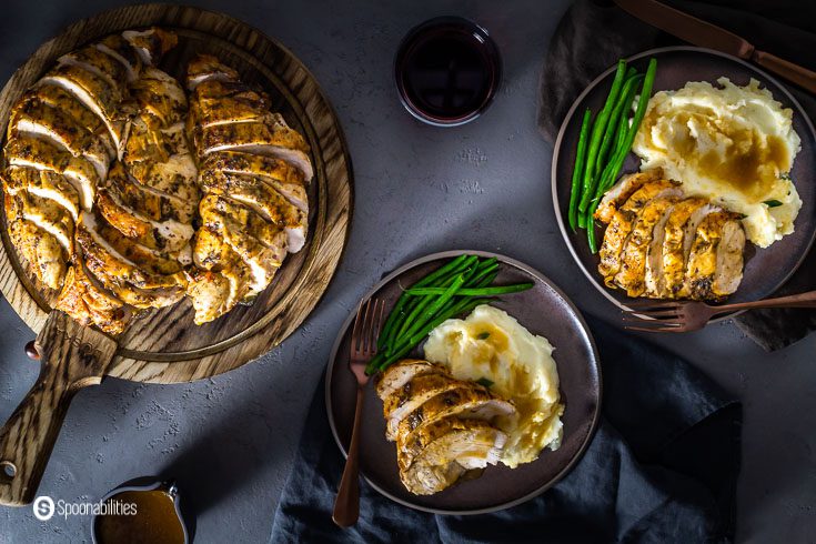 A table with Thanksgiving dinner for two. On the right top side of the photo a wooden board with roasted turkey breast and on the left side two round dark brown plates with turkey, mashed potatoes, and steamed green beans. recipe at Spoonabilities.com