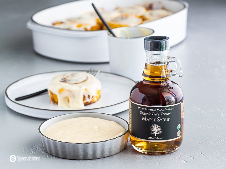 A glass botter of Organic Pure Vermont Maple Syrup and a small dish with the maple cream cheese icing on the left side. Recipe at Spoonabilities.com