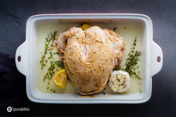 The bone-in and skin-on turkey breast seasoned with a mix of brown butter with chili and herbs. in the baking dish around the turkey with some rosemary and thyme springs, lemon juice, a whole head of garlic with the top off, and white wine. Recipe at Spoonabilities.com