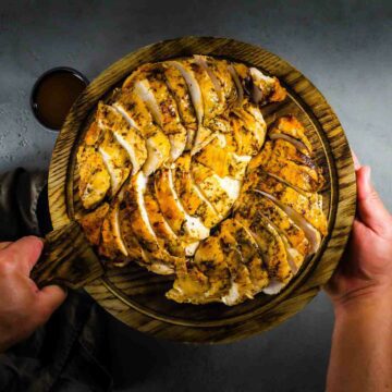 Recipe for Bone-in Turkey breast roasted and seasoned with red chili brown butter and herbs. Plated in a wooden board with two hands holding the wooden board. Recipe at Spoonabilities.com