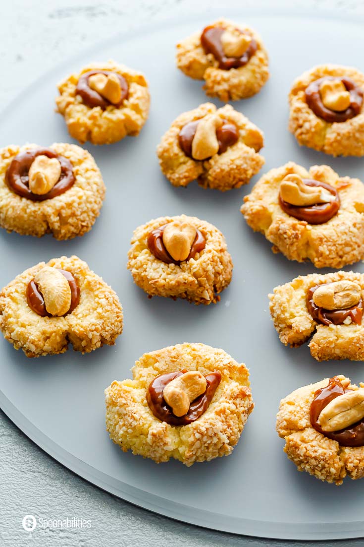 Close up of a thumbprint cookies filled with cinnamon Goat's milk caramel sauce and a whole cashew on top. Recipe at Spoonabilities.com