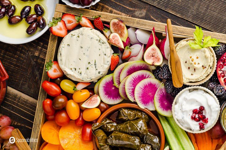 Wooden tray with cashew milk cheese with chives, dolma, plant-based tzatziki dip, cashew dip with roasted garlic, and fruits and vegetables. Recipe at Spoonabilities.com
