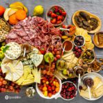 Overhead photo of a grazing table with a charcuterie board, cheeseboard, and gourmet products. Read more Charcuterie Board Ideas at Spoonabilities.com