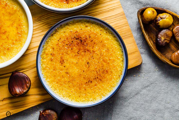 A blue ramekin with chestnut Crème brûlée in the center and two more ramekin on the top light side but you only can see a small corner of the ramekin. Recipe at Spoonabilities.com