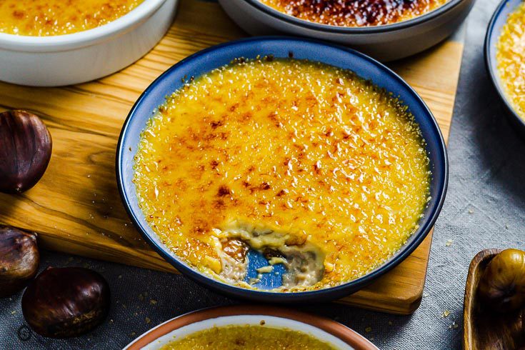 A blue ramekin with chestnut Crème brûlée and a piece out that you can see the creamy inside of the custard. Recipe at Spoonabilities.com