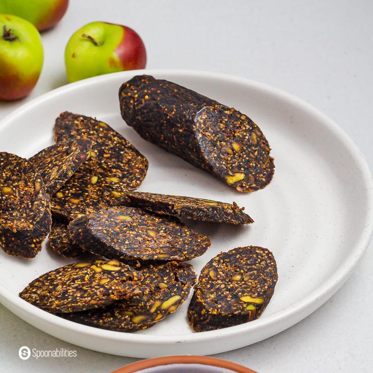 Fig salami with pistachio and pepper in a white plate. The fig salami is sliced in pieces. Product available at our shop at spoonabilities.com