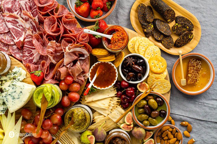 Charcuterie board recipe overhead view including olives, jams, and spreads in a wooden board. 