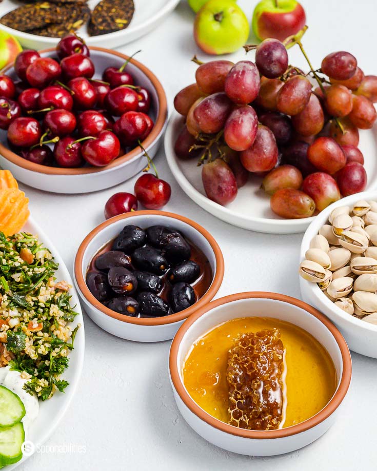 round flat bowl with honey and honeycomb near stuffed olives, grapes and cherries