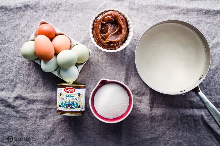The ingredients for the crème brûlée on a table with a grey tablecloth. Eggs, sugar, milk, heavy cream, and chestnut spread. Recipe at spoonabilities.com