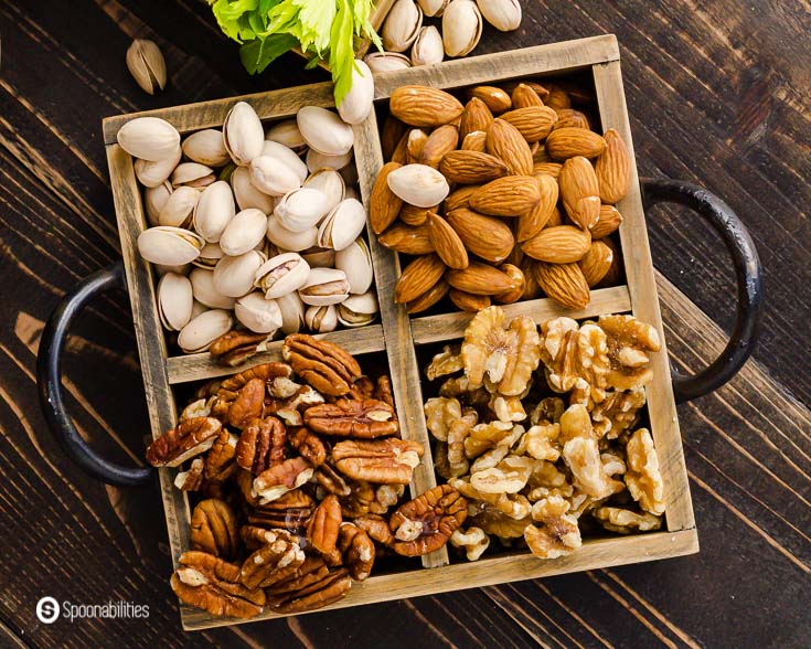 A wooden tray with almonds, walnuts, pistachios, and pecan. Recipe at Spoonabilities.com