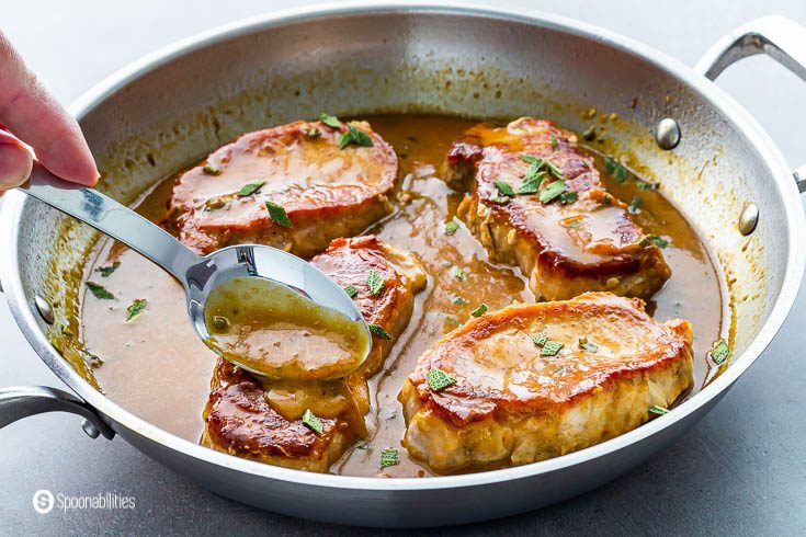 A hand pouring some of the apricot dijon mustard on top of a piece of pan-seared pork chops. Recipe at Spoonabilities.com