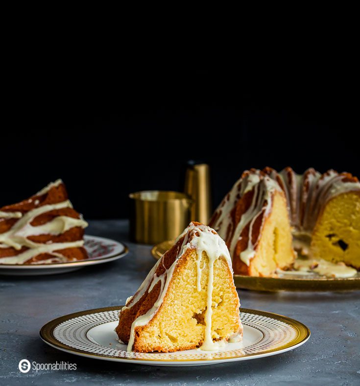 A piece of the eggnog cake on a plate and in the background the whole Bundt cake with a brandy and eggnog flavor. Recipe at Spoonabilities.com