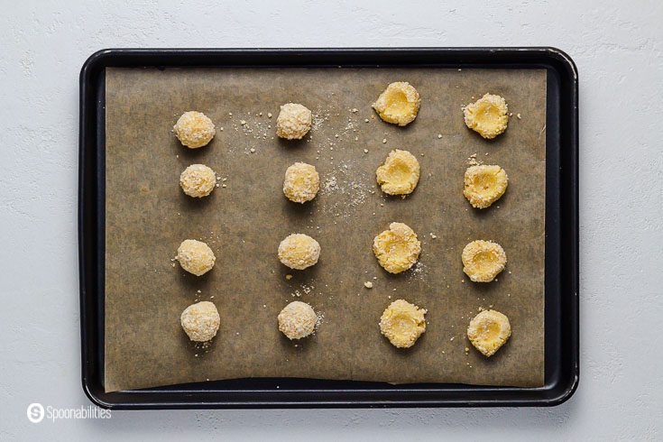 Cookies in the baking tray with some with the thumbprint in the center and others still like a ball. Recipe at Spoonabilities.com